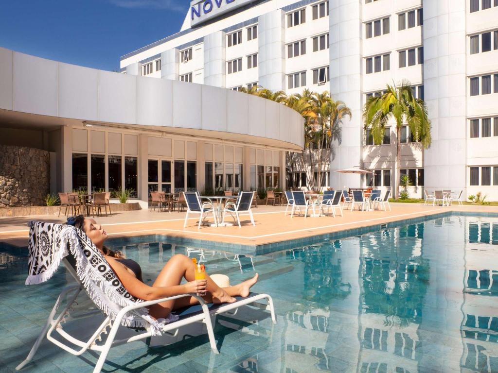 a woman sitting in a chair next to a swimming pool at Novotel Sao Jose dos Campos in São José dos Campos