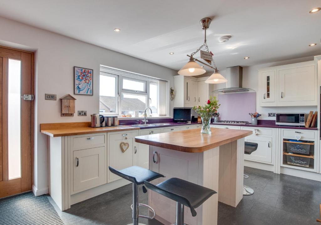 a kitchen with white cabinets and a island with two stools at 5 The Fairway in Braunton