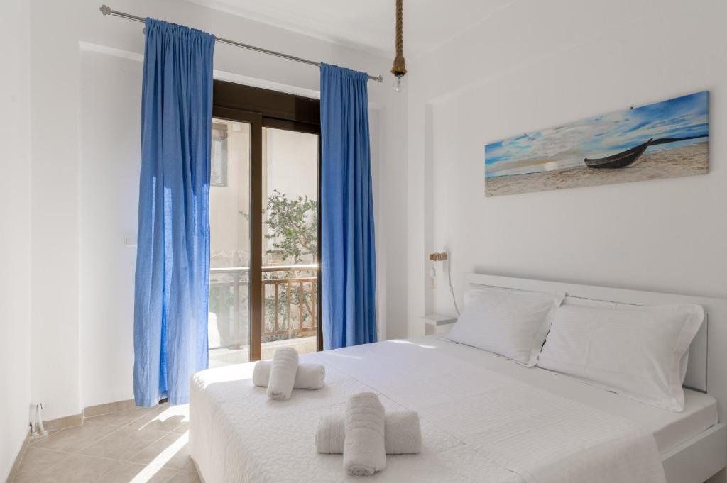 a bedroom with a white bed with blue curtains and a window at Zandre shiny apartment in Nea Potidaea