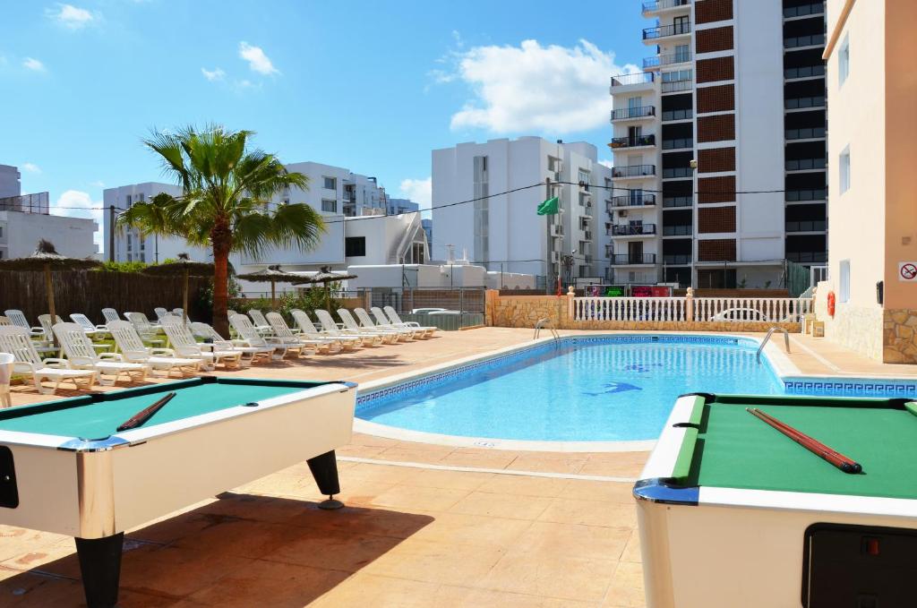 
a beach with a pool, chairs, tables and a tennis court at Hotel Apartamentos Vibra Central City in San Antonio
