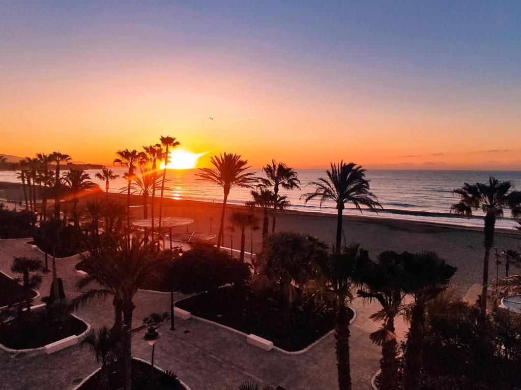 Una puesta de sol sobre una playa con palmeras y el océano. en Estepona primera línea de playa, apartamento 2-4 personas, en Estepona