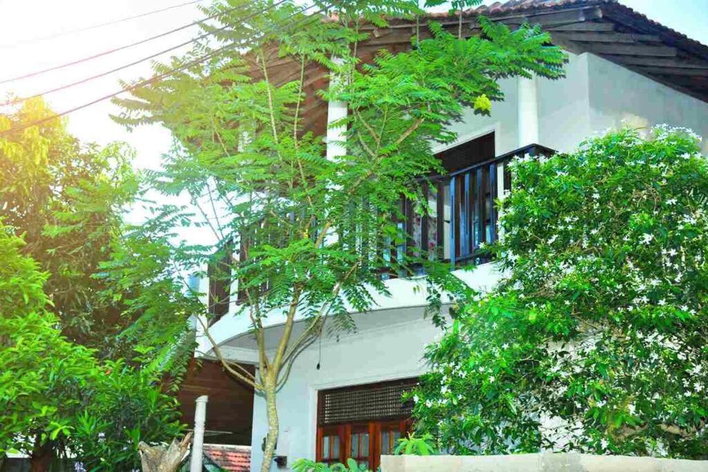 a building with a balcony and trees in front of it at Sunil Homestay in Tangalle