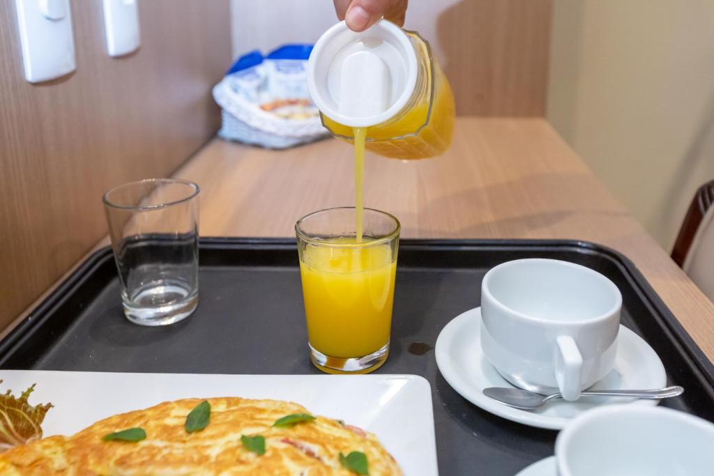a person pouring orange juice from a jug into a glass at Rio Aeroporto Hotel Galeão in Rio de Janeiro