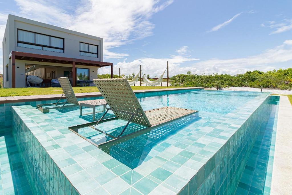 una piscina con 2 sillas y una casa en SA05 Excelente Casa 5 Suítes - Condomínio Reserva de Sauípe en Costa do Sauipe