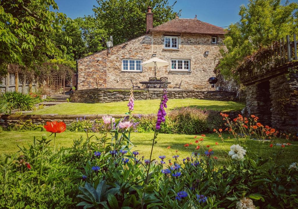 a garden in front of a stone house with flowers at Court Cottage in Berrynarbor