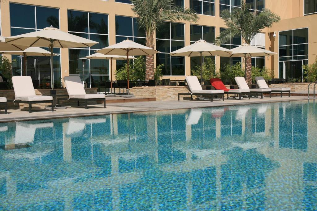 a swimming pool with chairs and umbrellas next to a building at Centro Yas Island-by Rotana in Abu Dhabi