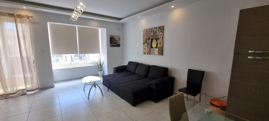 a living room with a black couch and a window at VBH APARTMENT PACEVILLE ST. JULIAN'S in Paceville