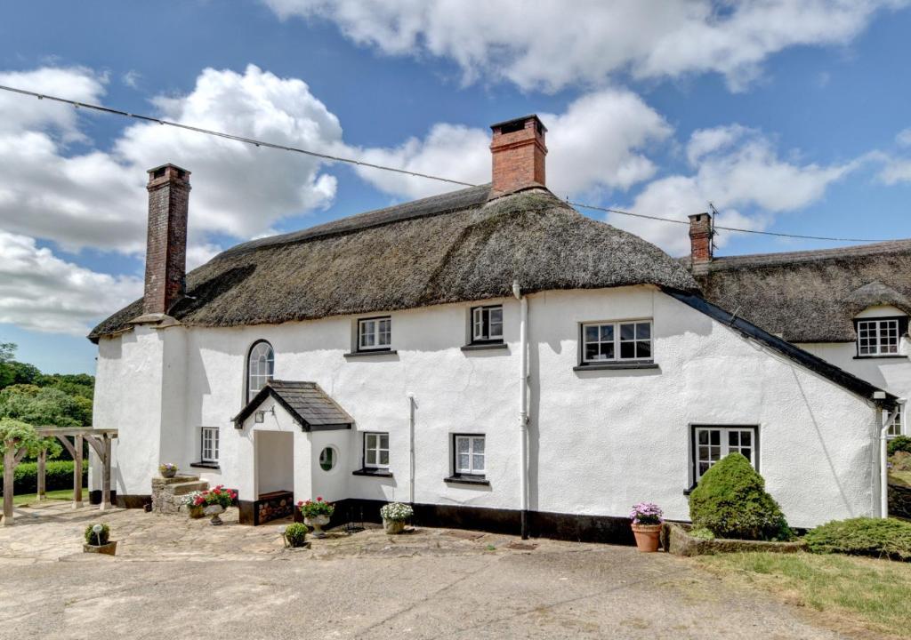 an old white cottage with a thatched roof at Nethercott Manor in Rose Ash