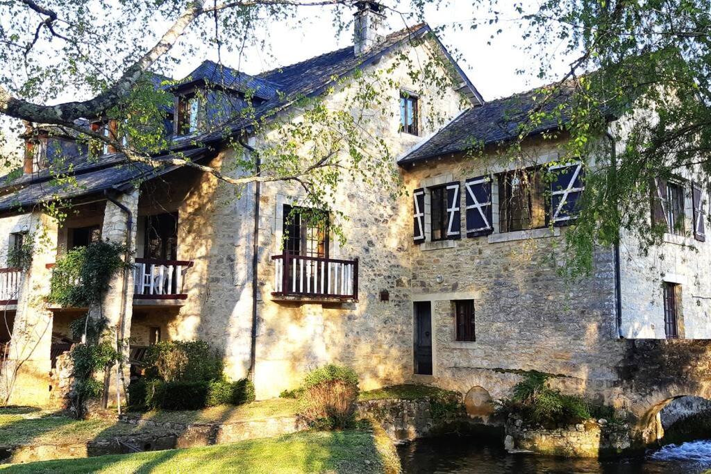 uma antiga casa de pedra com um rio em frente em Le Moulin de la Rode em Coly