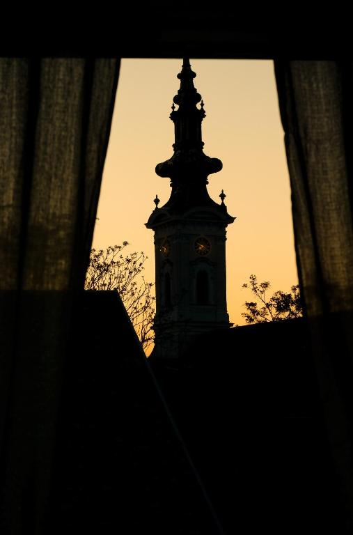 una torre dell'orologio in lontananza con il tramonto sullo sfondo di San Lux Dunavska a Novi Sad