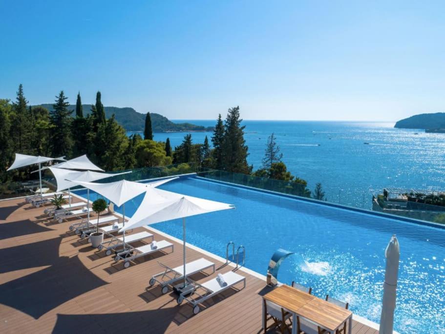 einen Pool mit weißen Sonnenschirmen und dem Meer in der Unterkunft Two-bedroom luxury apartment 2 mins to the sea in Budva