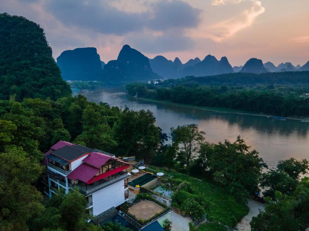 una casa en una colina junto a un río con montañas en Yangshuo River Lodge Hotel en Yangshuo