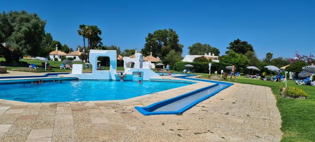 uma piscina num resort com pessoas sentadas à sua volta em Pedras D'el Rei - Relax Estúdio em Tavira