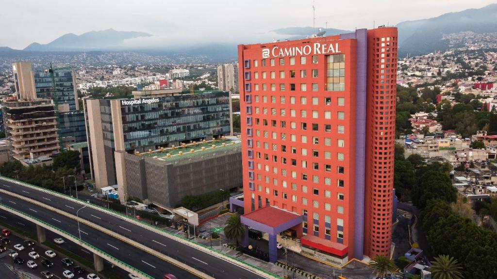 um edifício alto e vermelho com uma placa ao lado de uma auto-estrada em Camino Real Pedregal Mexico em Cidade do México