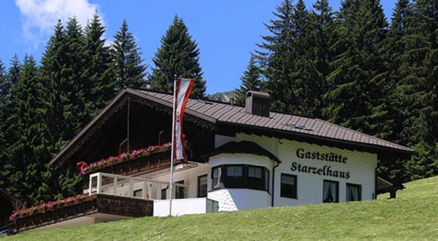 ein Haus auf einem Hügel mit einer Flagge davor in der Unterkunft Gasthof Starzelhaus in Mittelberg