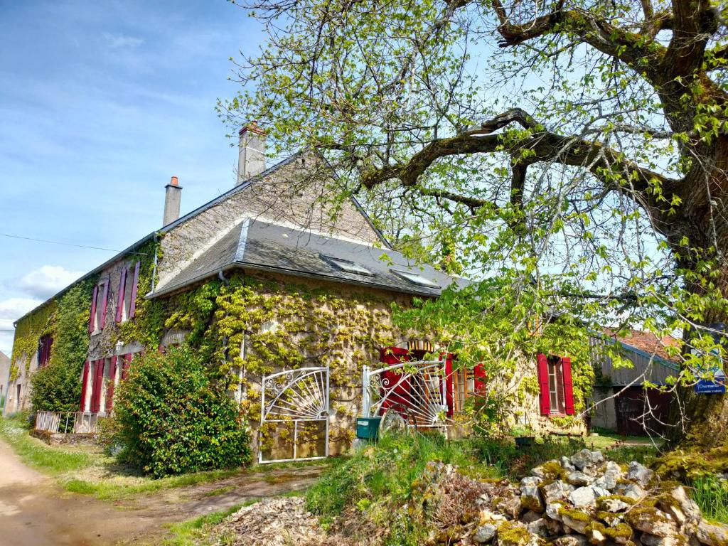 una antigua casa de piedra con ventanas rojas y hiedra en La ferme des douceurs, en Cervon