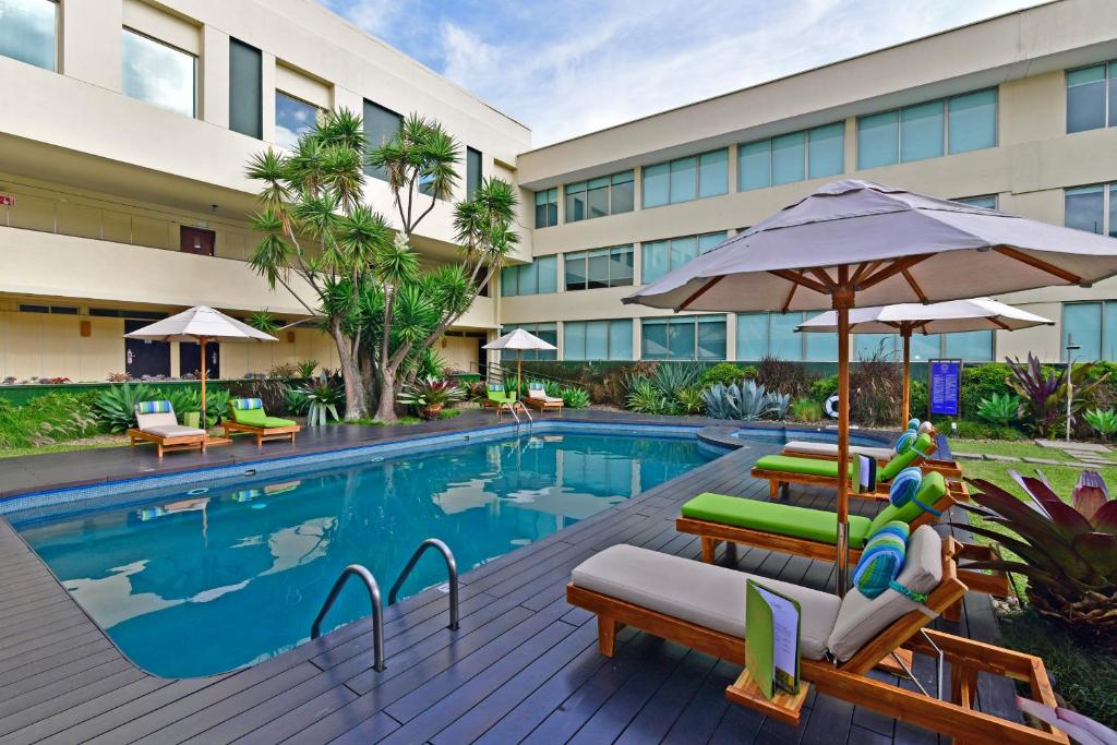 a hotel pool with chairs and an umbrella at Auténtico Hotel in San José