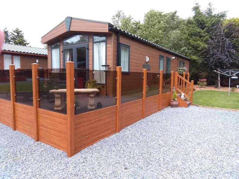 a house with a wooden fence with a patio at Silver Birch Lodge in Auchterarder