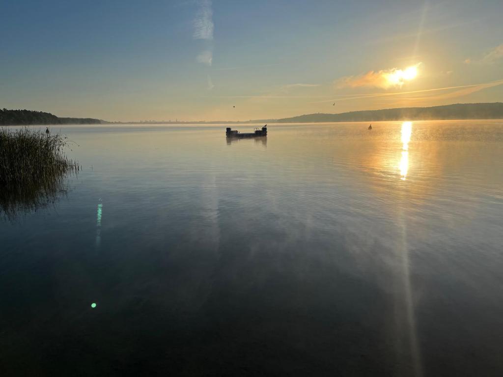 un barco en medio de un lago al atardecer en FeWo mit 3 SZ, direkte Innenstadtlage, Südterrasse, Parkplatz auf dem eigenem Privatgrundstück, 2x E-Bike und E-Autoladesäule inklusive, Konzertkirche, Schauspielhaus, FH, Jahnsportforum sowie der Tollensesee sind fußläufig in ein paar Minuten erreichbar en Neubrandenburg