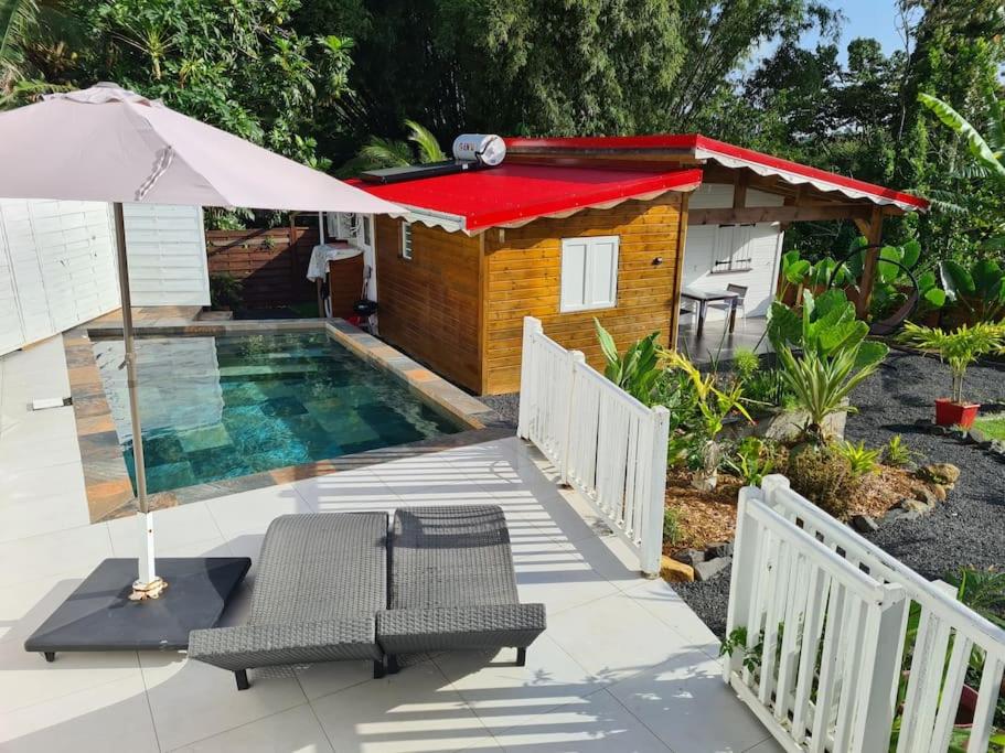 a small house with a swimming pool and an umbrella at Maison de campagne avec piscine et spa in Lamentin