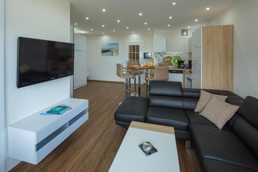 ein Wohnzimmer mit einem schwarzen Sofa und einer Küche in der Unterkunft Prinz Hamlet App. 16  in Neustadt in Holstein