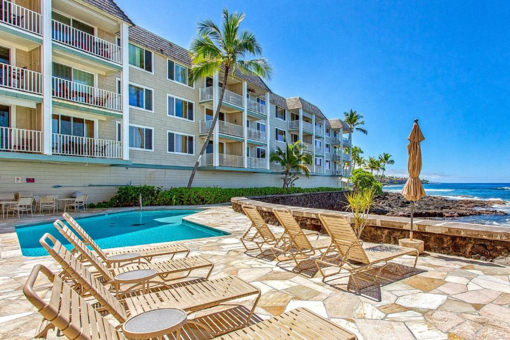 a resort with chairs and a swimming pool and the ocean at Beautiful Oceanfront Welcomes you at Hale Kona Kai 203 by Casago Kona in Kailua-Kona