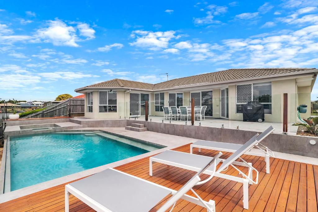 a house with a swimming pool and two chairs on a deck at Breathtaking 4BR Resort like House Right Near Wurtulla Beach With Infinity Pool in Kawana Waters