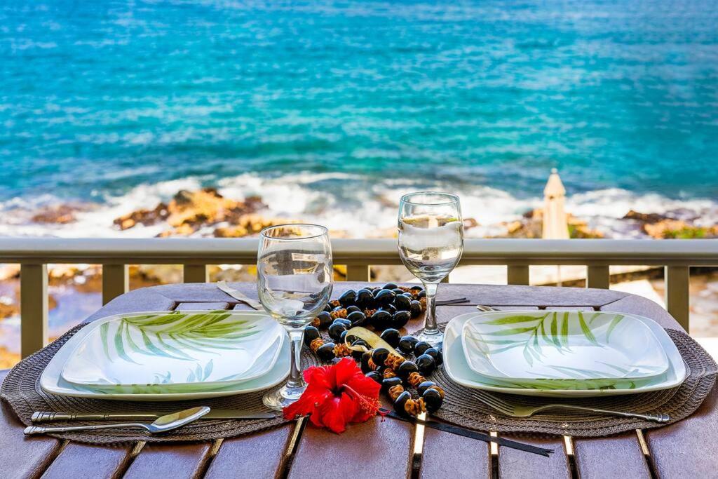 a table with two plates and wine glasses on the beach at Dreamy True Oceanfront Condo - Hale Kona Kai 307 by Casago Kona in Kailua-Kona