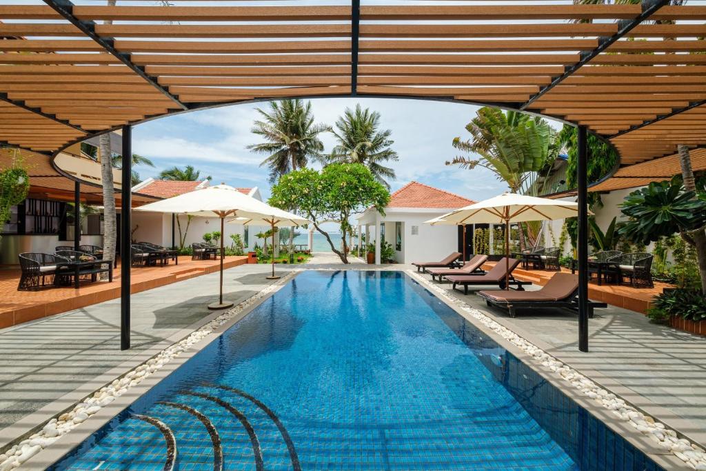 uma piscina exterior com cadeiras e guarda-sóis em Tuong Boutique Resort Mui ne em Mui Ne