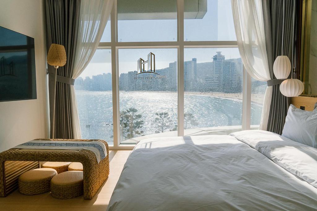 een slaapkamer met een groot raam met uitzicht op het water bij De Homme Hotel in Busan