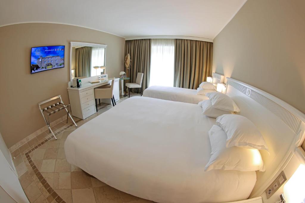 a hotel room with a large white bed and a desk at Hôtel L'Abbaye in Calvi
