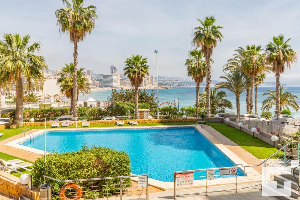 a swimming pool with palm trees and the ocean in the background at Apartamento Mesana 13 - Grupo Turis in Calpe