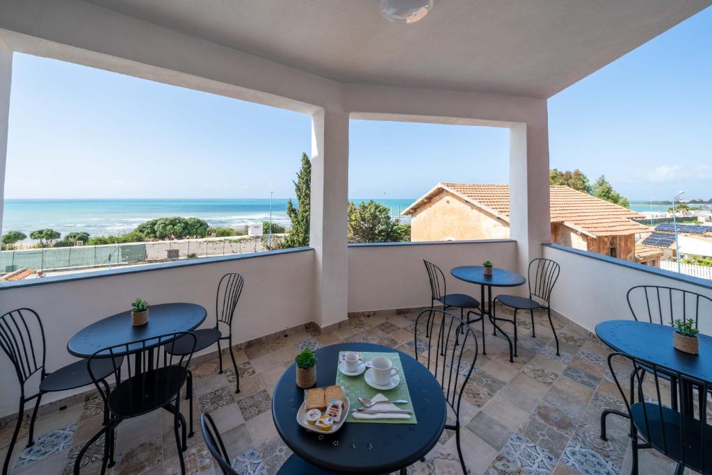 uma varanda com mesas e cadeiras e vista para o oceano em Le Camere della Scala em Porto Empedocle