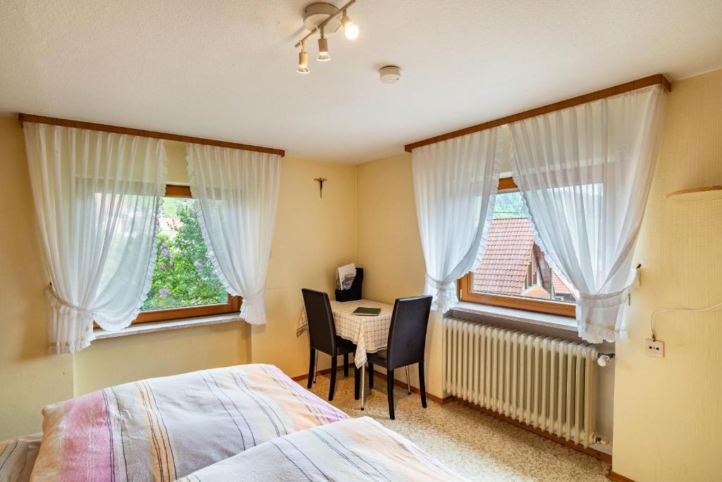 ein Schlafzimmer mit einem Bett, einem Tisch und zwei Fenstern in der Unterkunft Bergblick in Forbach