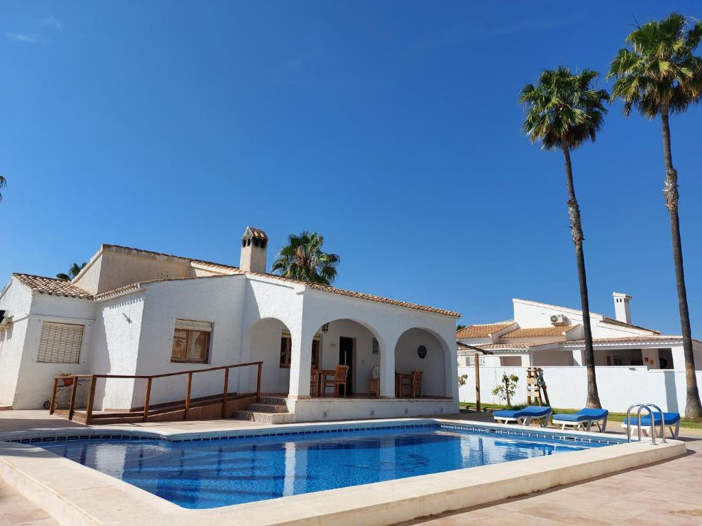 a villa with a swimming pool and palm trees at ZENIA HOSTEL in Playa Flamenca
