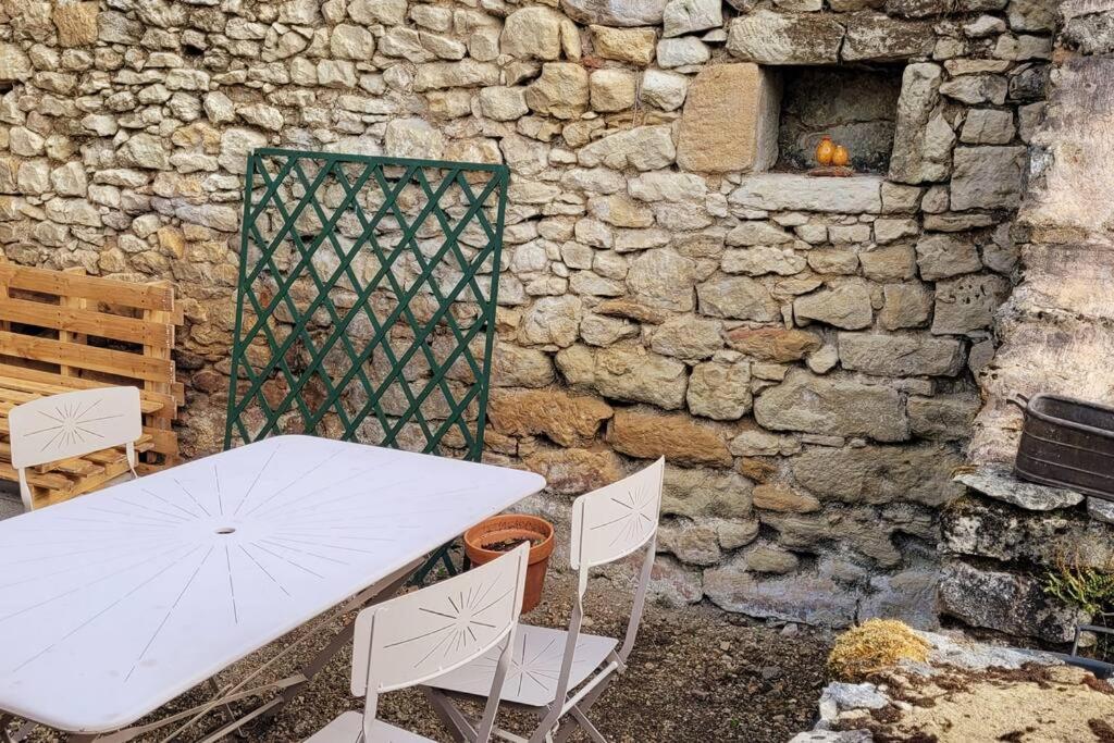 a white table and chairs next to a stone wall at Maison périgourdine avec vue et piscine chauffée in Peyzac-le-Moustier