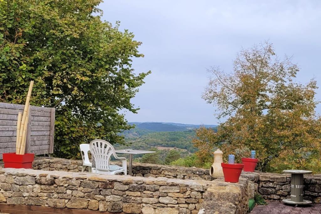 a stone wall with two chairs and a table on it at Maison périgourdine avec vue et piscine chauffée in Peyzac-le-Moustier