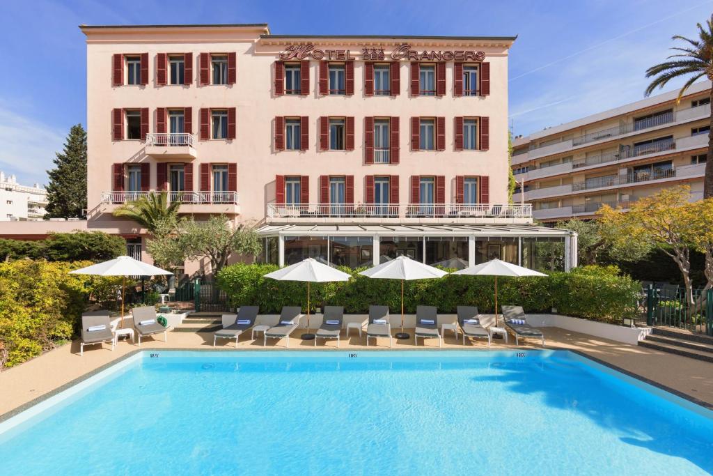 坎城的住宿－The Originals Boutique, Hôtel des Orangers, Cannes (Inter-Hotel)，大楼前的带椅子和遮阳伞的游泳池