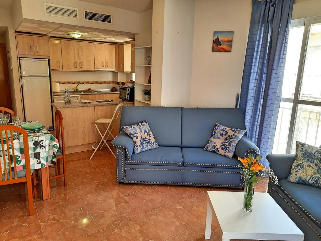 Una sala de estar con un sofá azul y una cocina. en Apartamento playero con vistas a la montaña, en Castell de Ferro