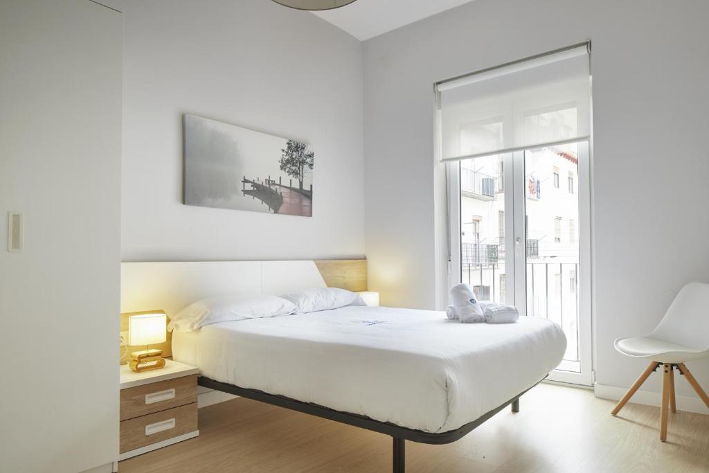 a white bedroom with a bed and a window at Aiztondo - Basque Stay in San Sebastián