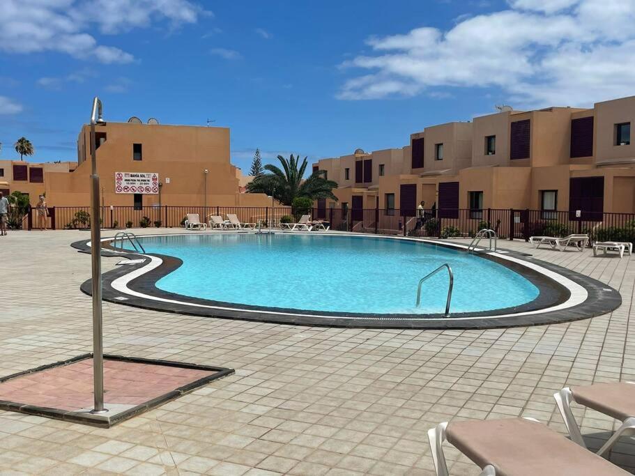 a swimming pool in a courtyard with chairs and buildings at Elisabeth Apartmant in Caleta De Fuste