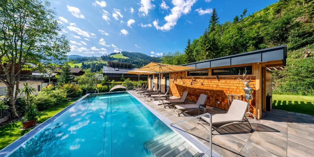 a swimming pool with chairs and a house at Luxusapartment Müllerhaus in Mühlbach am Hochkönig