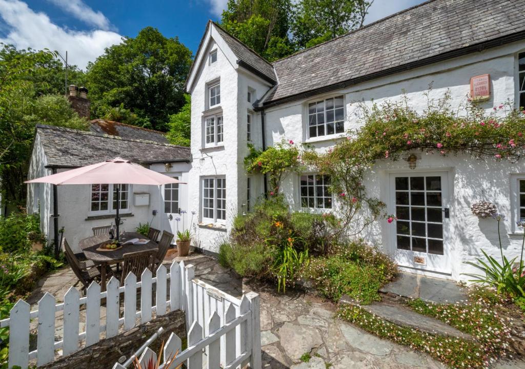 a white house with a white fence and a table and an umbrella at Well Too in Helford