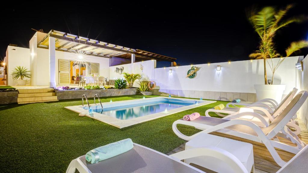 a backyard with a pool and chairs and a house at Villa Amatista Salinas Golf & Beach in Caleta De Fuste