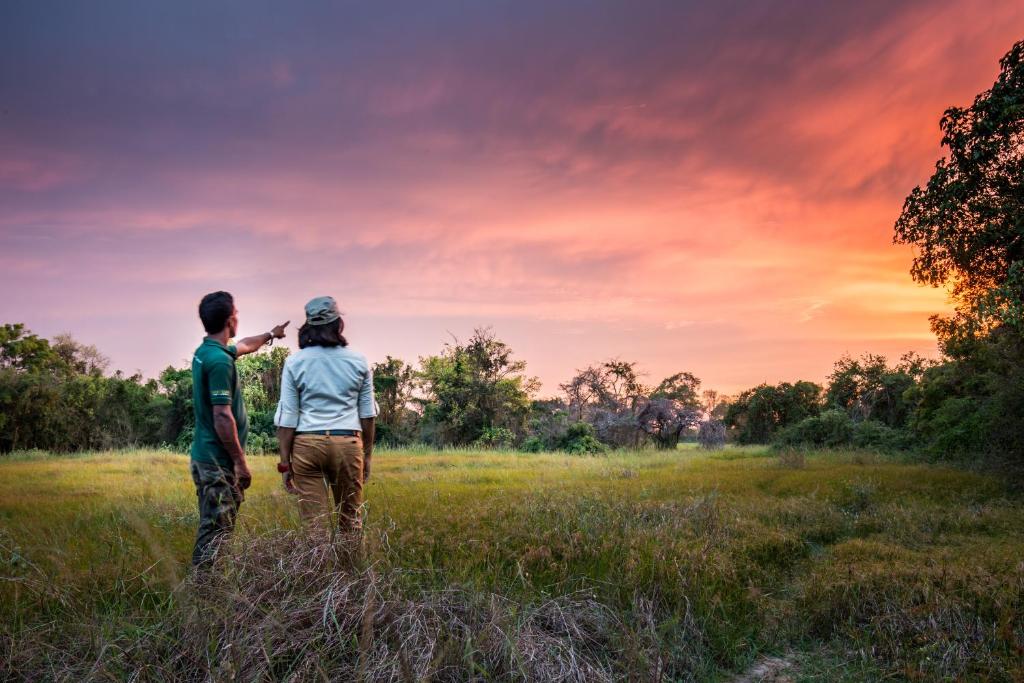 a man and woman standing in a field at sunset at Mahoora Wilpattu - by Eco Team in Wilpattu