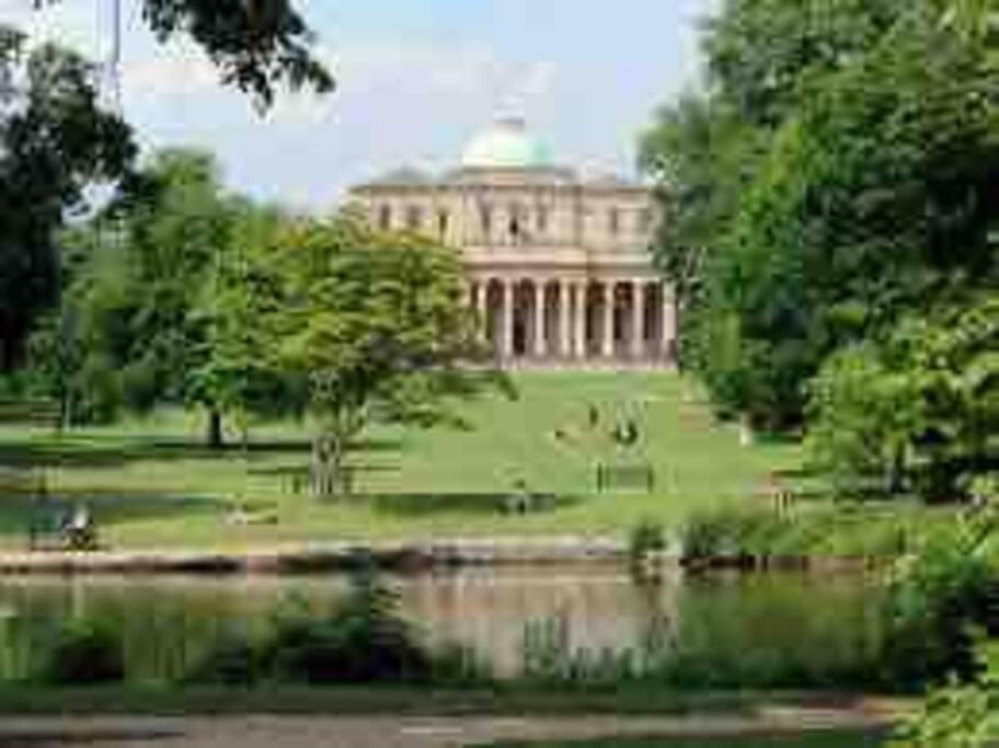 a large building in the middle of a park with a lake at 5 Bed Modern Cheltenham Town Centre Home in Cheltenham