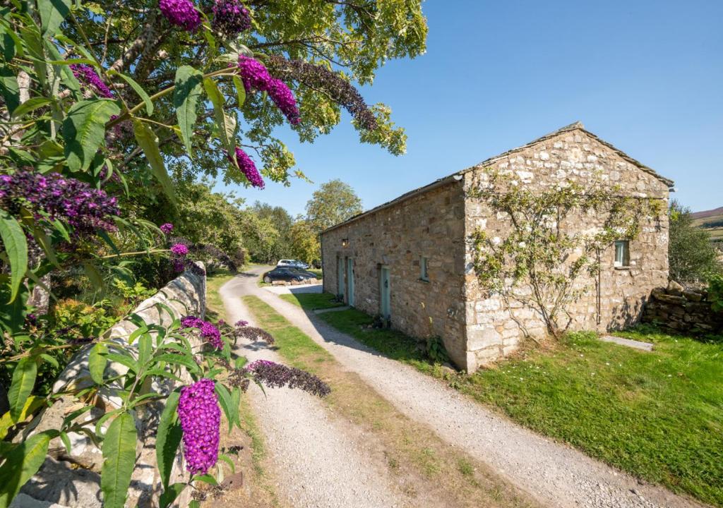 un edificio in pietra con fiori viola accanto a una strada di Bizzys Bolthole a Reeth