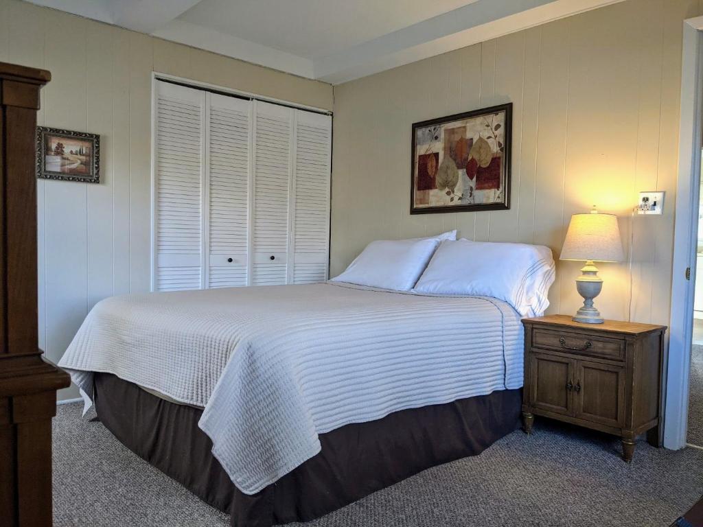 ein Schlafzimmer mit einem weißen Bett, einem Nachttisch und einem Fenster in der Unterkunft Casual Living Extended Stay Hotels in Algonquin