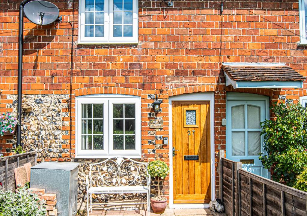 a brick house with a wooden door and a bench at Flint Cottage in Debenham