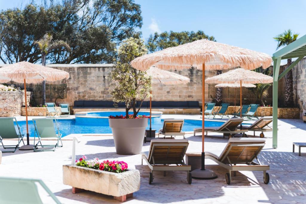 un patio con sedie, ombrelloni e piscina di Ogygia Suites Gozo a Għarb